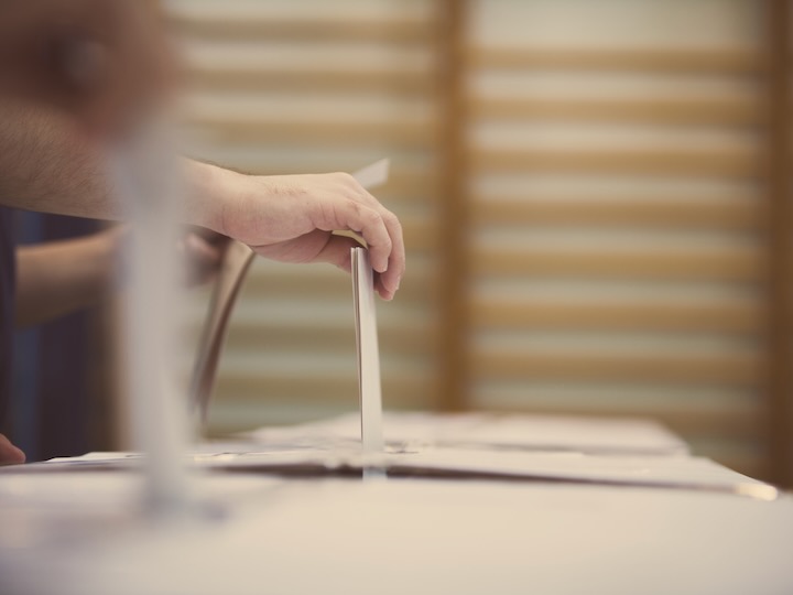 Hands place ballots into a row of ballot boxes during an election.