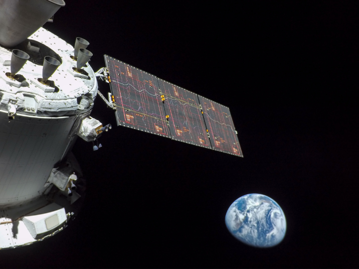 Spacecraft with extended solar panel orbits with Earth visible in the distance against the blackness of space.