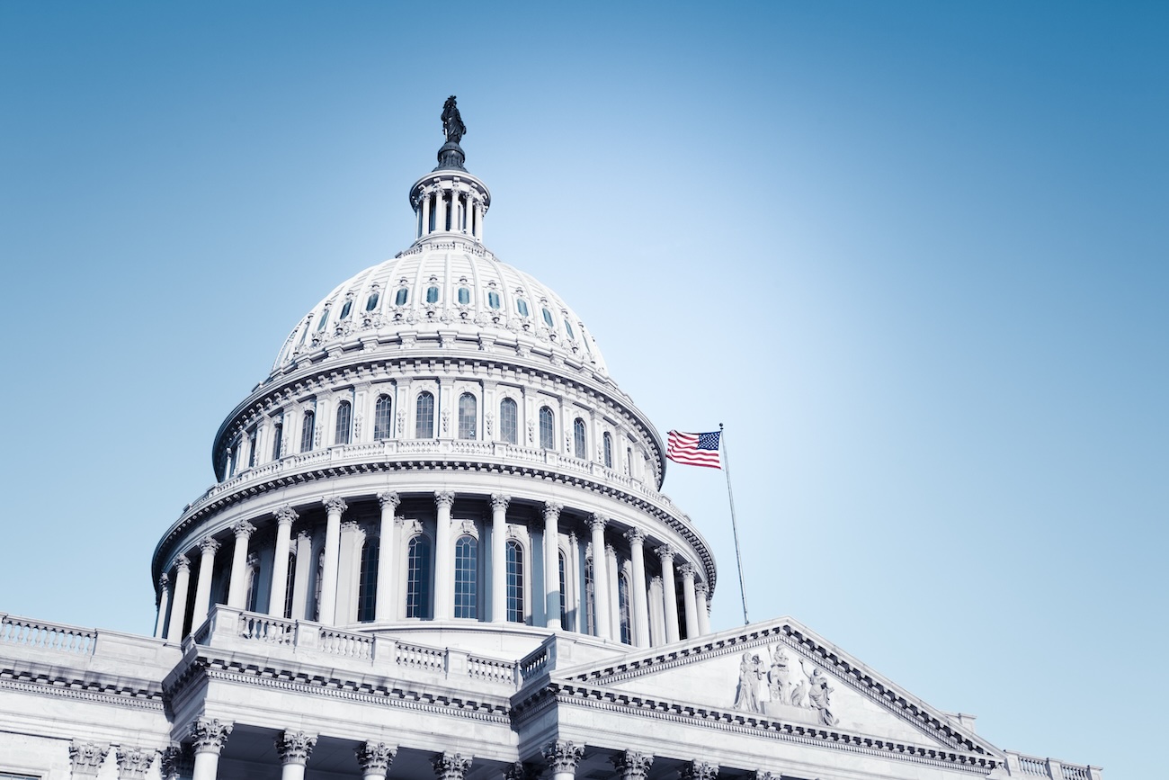 U.S. Capitol dome with an American flag flying against a clear blue sky.