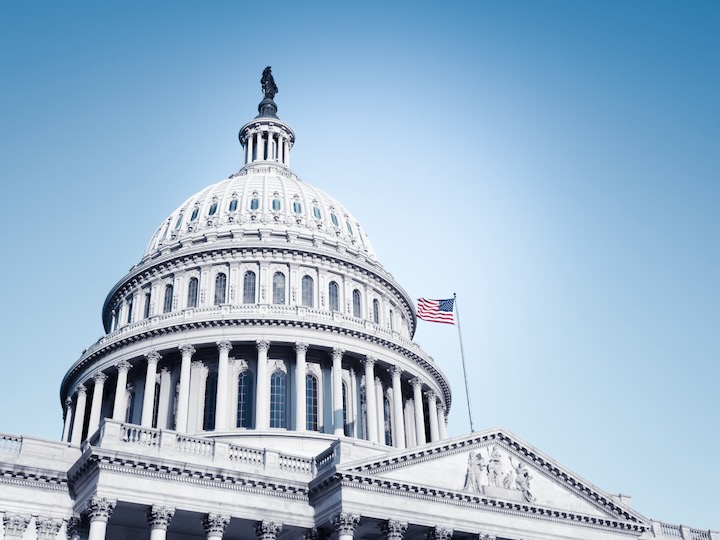 U.S. Capitol dome with an American flag flying against a clear blue sky.