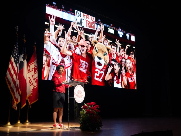 woman on stage with sign image of uh athletics behind her