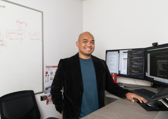 Portrait of Mark Rosanes smiling at his standing desk.