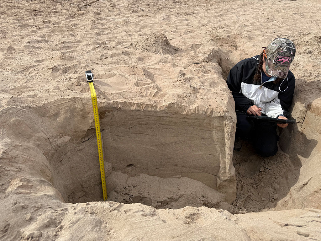 Student crouched in trench to take photos of crossbedding structures. Photo credit: Brooke Pryor