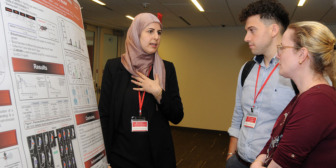 student researcher at poster talking with attendees