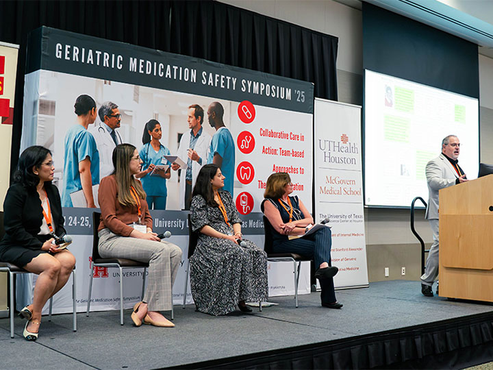 three people seated and fourth person at podium on stage