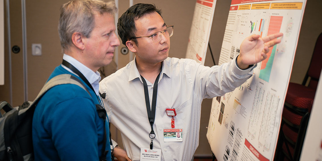 student researcher gesturing to poster with attendee
