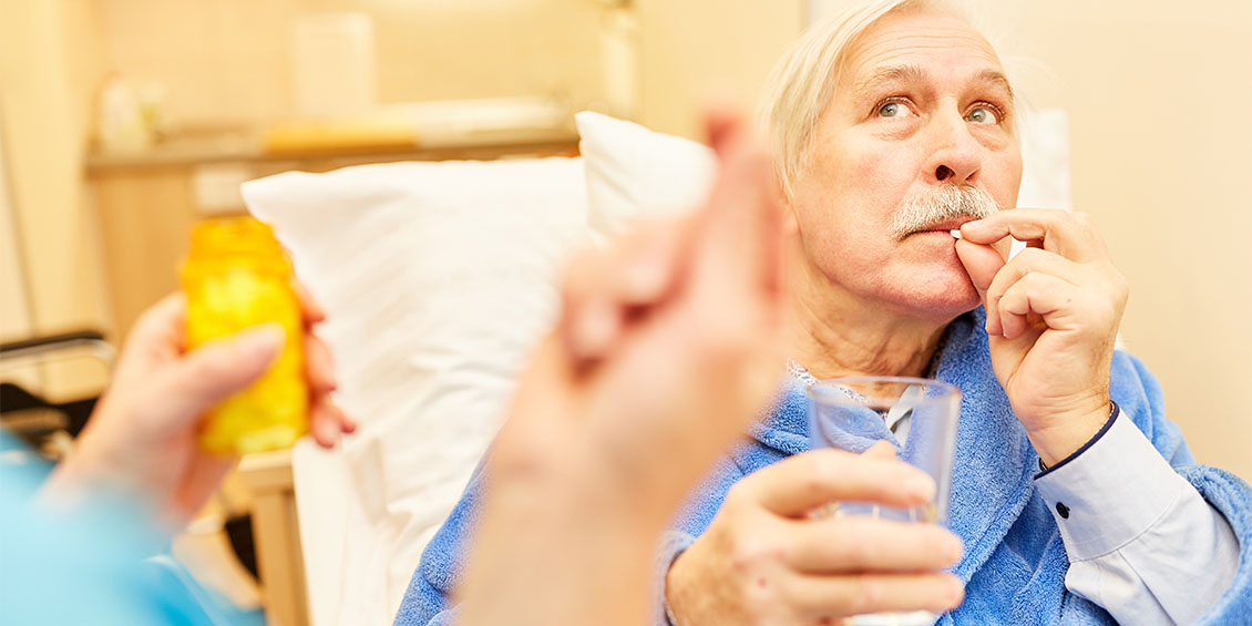 older man taking pill as someone looks on