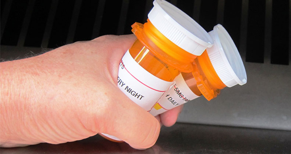 hands holding pill bottles next to bin