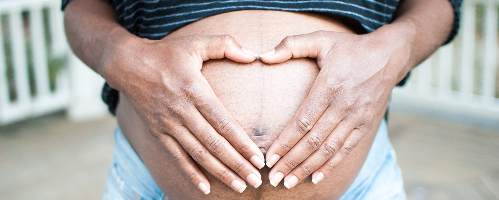 a pregnant belly with hands forming a heart over the belly button