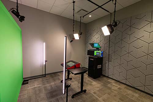 A media room with sound-proofed walls, a green screen, lighting and computer consoles.