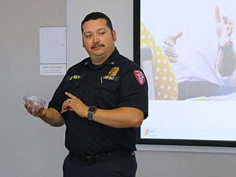 A Hispanic man stands in front of a projection screen a points to a transparent CPR oxygen mask with a value.