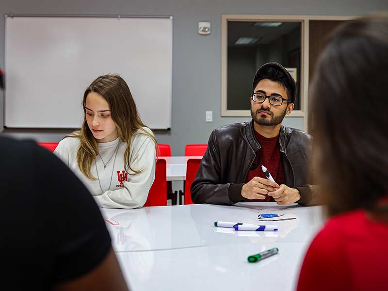 Students sit at a desk taking notes while listening to discussion.