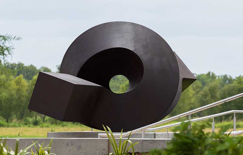 Photograph of rear of a metal sculpture looking through the spiral of a rectangular prism that twists in a loop.