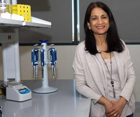 A dark-haired woman smiling while standing next to laboratory equipment