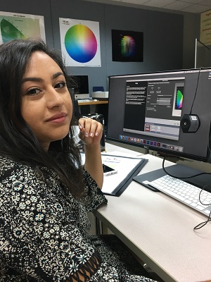 Portrait of a Hispanic woman sitting in front of a computer screen while using editing software.