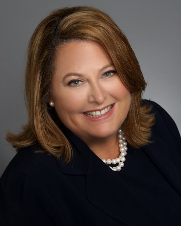 Portrait of a woman smiling in a black jacket wearing a white pearl necklace