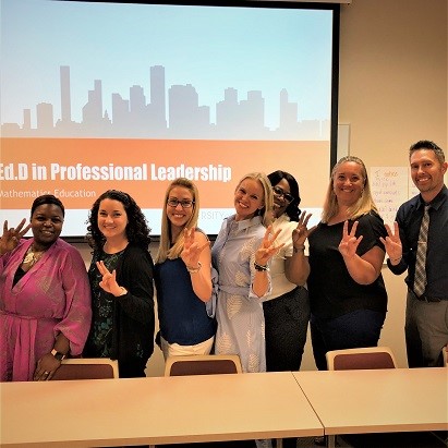 Group of students and instructor posing with the university's hand sign