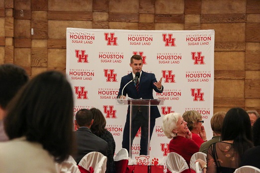 A man in a suit behind a podium excitedly speaks to an audience