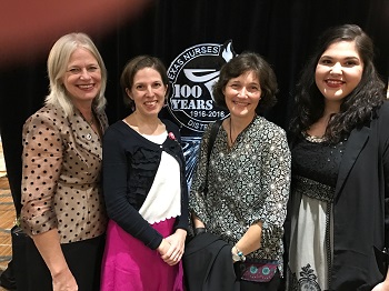 Four women stand together smiling.