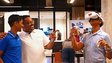 A school kid uses virtual reality equipment while his parent and sibling watch.