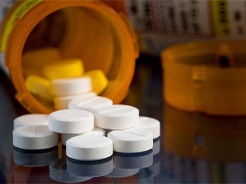 Close up of a transparent orange bottle of medicine lying on its side. A pile of small cylindical tablets of medicine spill out of the bottle.