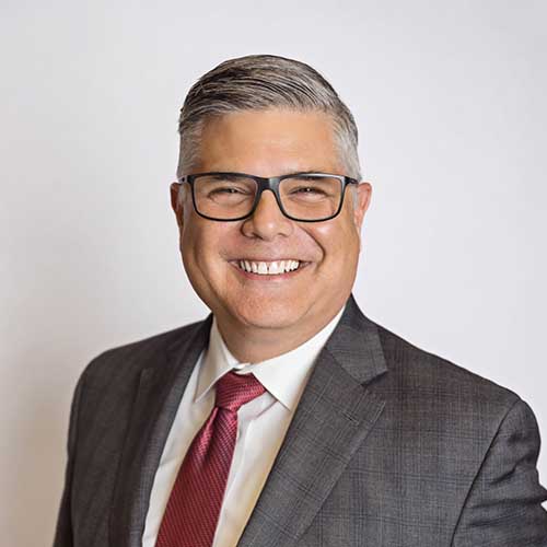 Portrait of white man smiling with glasses in a gray suit and red tie