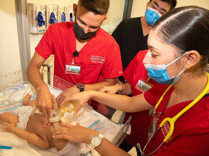 Two nursings students attend to a pediatric manikin in a hospital bassinet.