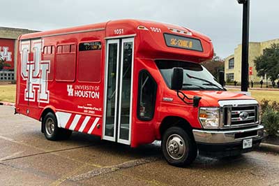 A red shuttle bus with a large UH logo parked on a street