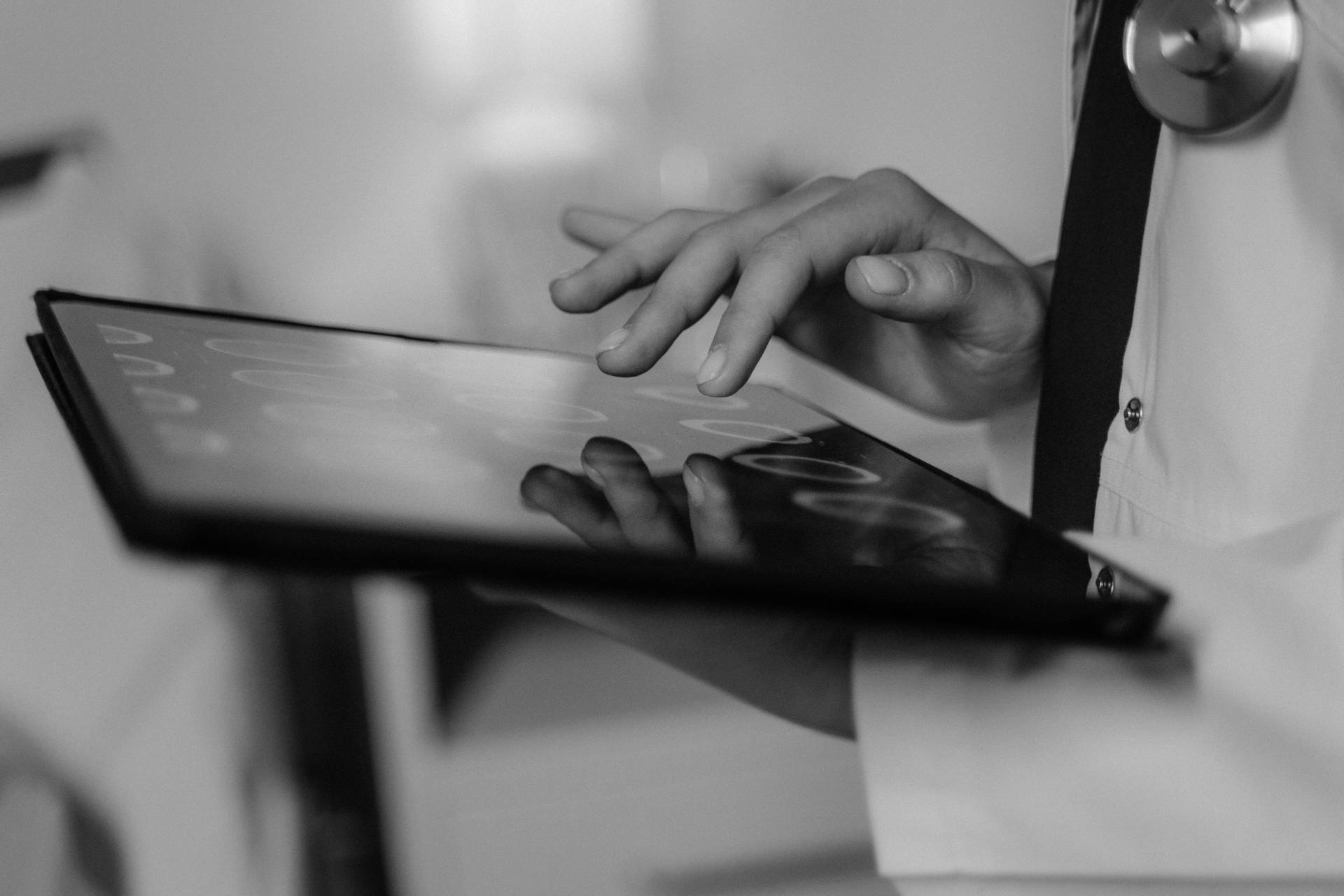 Person using a touchscreen tablet while wearing a white coat, with a close-up view of their hand interacting with the screen.